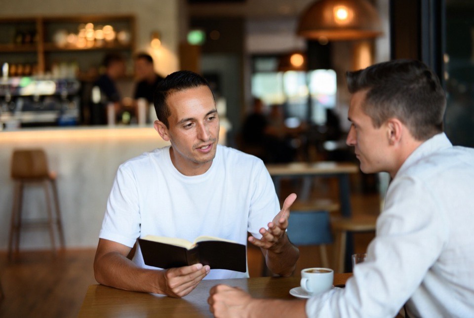 Two leaders talking over an open Bible in a café